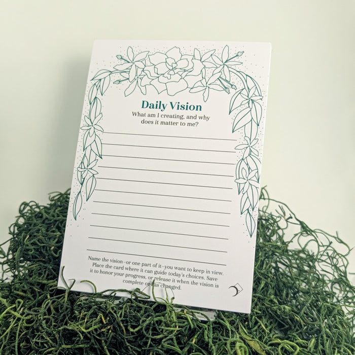 A Daily Vision notepad with a green botanical leaf border, displayed on a bed of green moss against a white background.